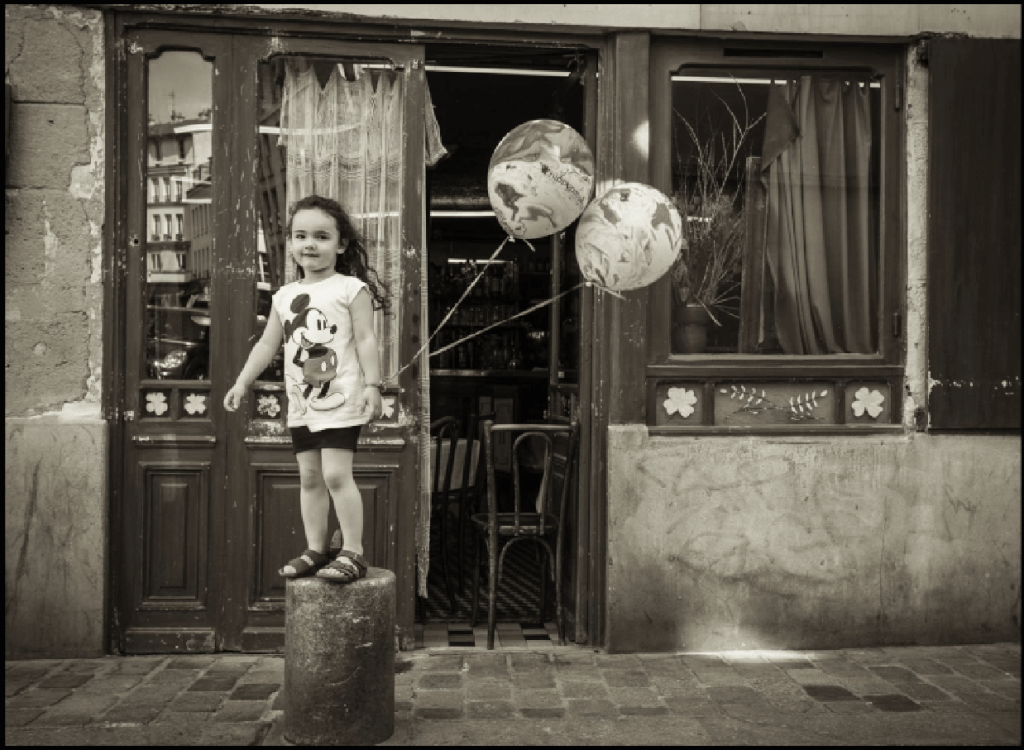 This little girl was running down the street and jumped up on the pillar with her balloons, full of energy, and turned toward me. When the camera was seen... you get it.