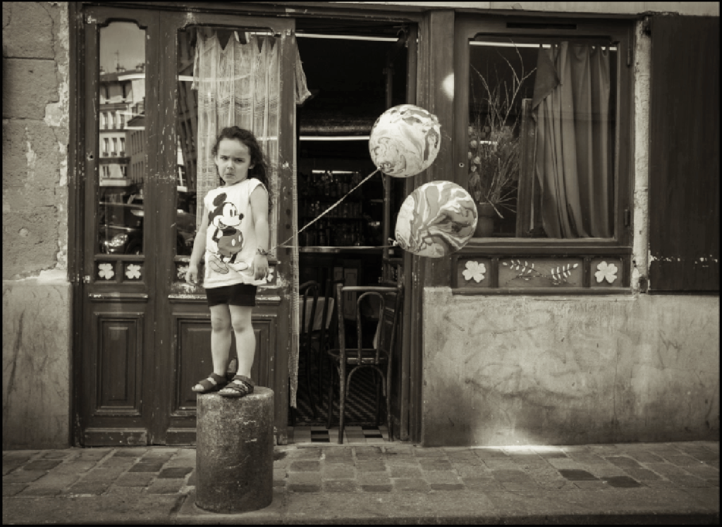 This little girl was running down the street and jumped up on the pillar with her balloons, full of energy, and turned toward me. When the camera was seen... you get it.